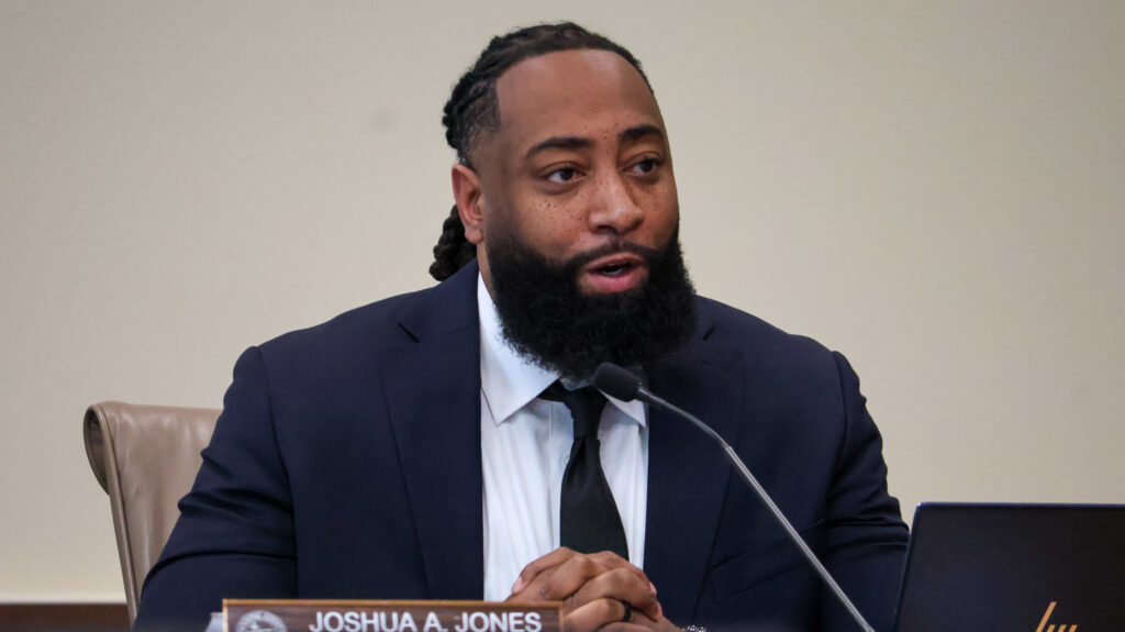 Sandoval County Commissioner Joshua A. Jones sitting behind a desk, speaking into the microphone.