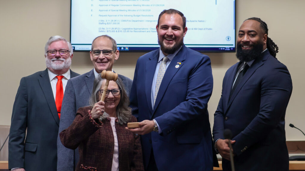 Sandoval County Commissioners gathering around, all laughing, with Commissioner Bruch standing in the middle, holding up a gavel.