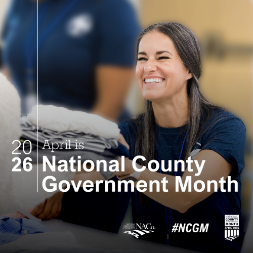 April is National County Government Month, as indicated by text on the image. A smiling person is handing a stack of folded clothes to another person, with the NACo logo and #NCGM hashtag visible.
