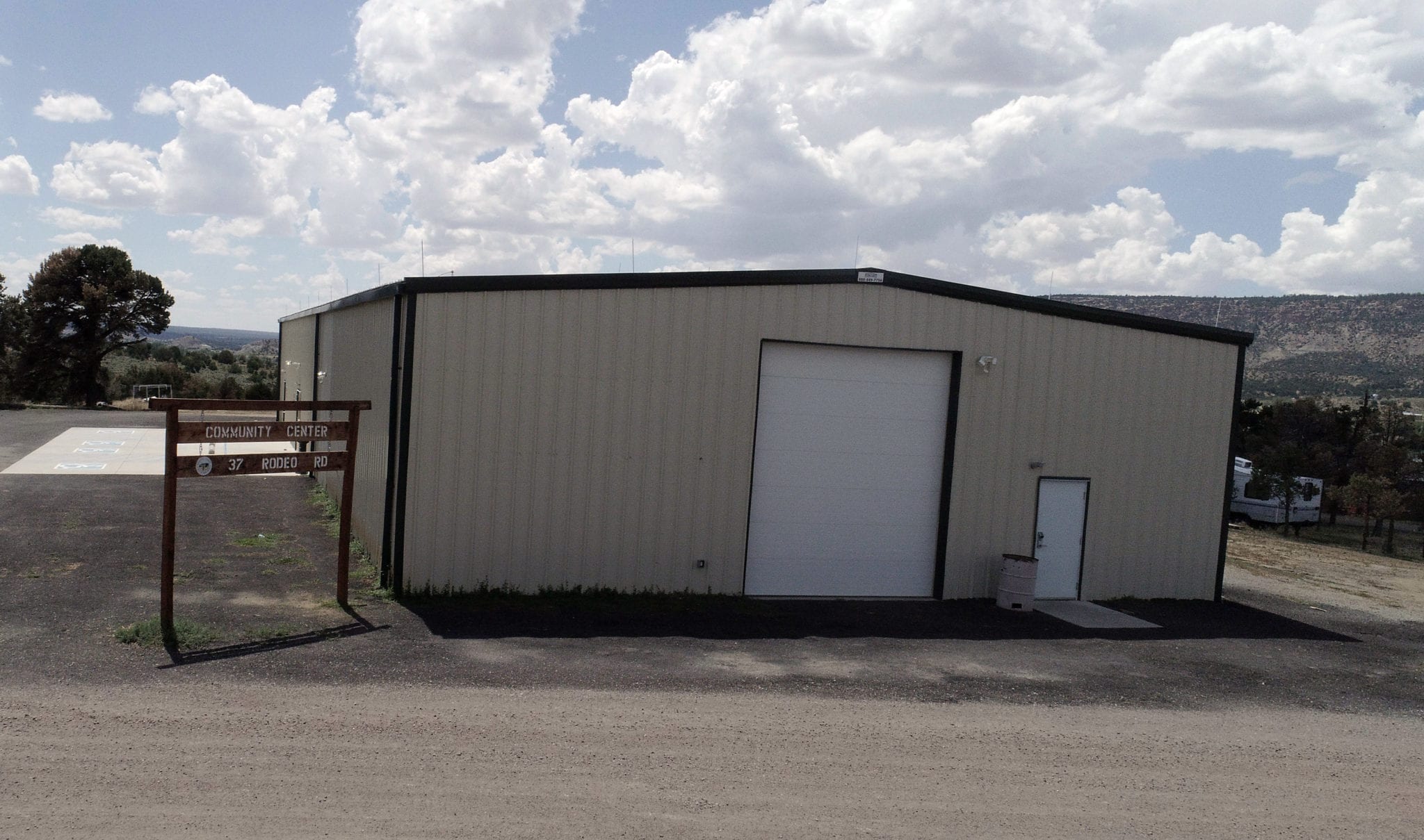 Exterior of the Sandoval County Fairgrounds Community Center building at 37 Rodeo Road, a metal structure with a large roll-up door and a wooden roadside sign
