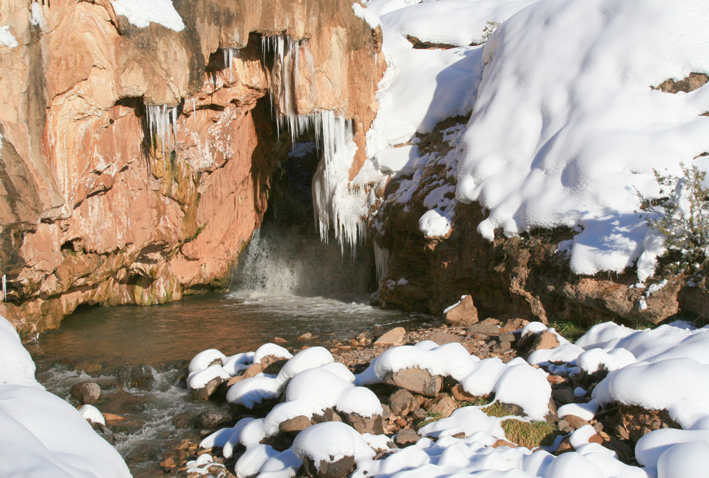sodadam Soda Dam near Jemez Springs in winter, with a waterfall flowing through the red mineral travertine formation and snow blanketing the surrounding rocks.