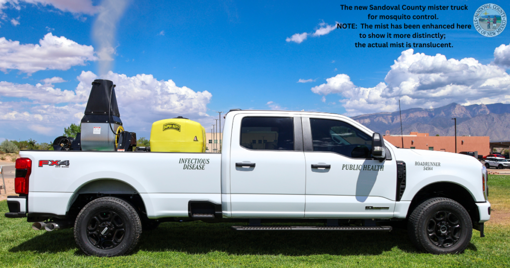 White public health pickup truck equipped with a mosquito mister and yellow tank spraying a visible translucent mist against a blue sky with clouds.